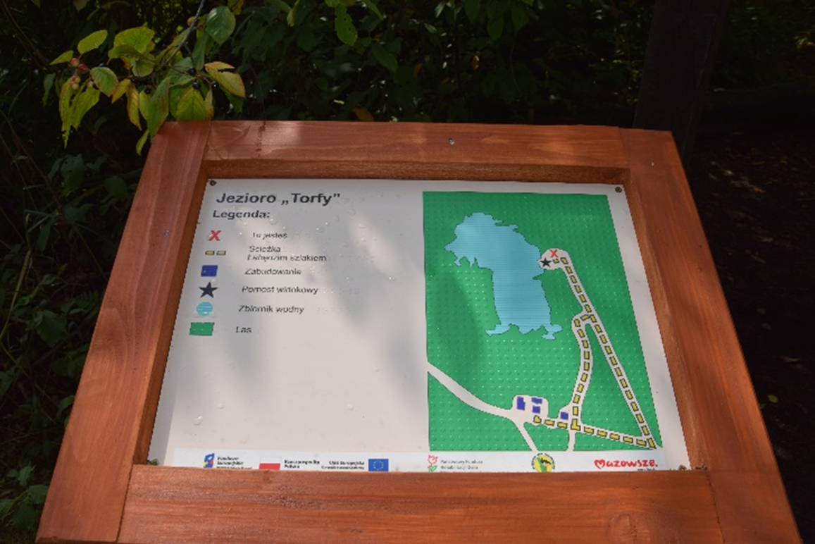 Makieta tyflograficzna Jezioro "Torfy" w drewnianej ramie stojąca na zewnątrz.