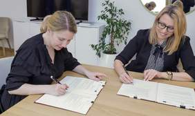 Pokaż zdjęcie: Dwie kobiety siedzące przy stole podpisują dokumenty